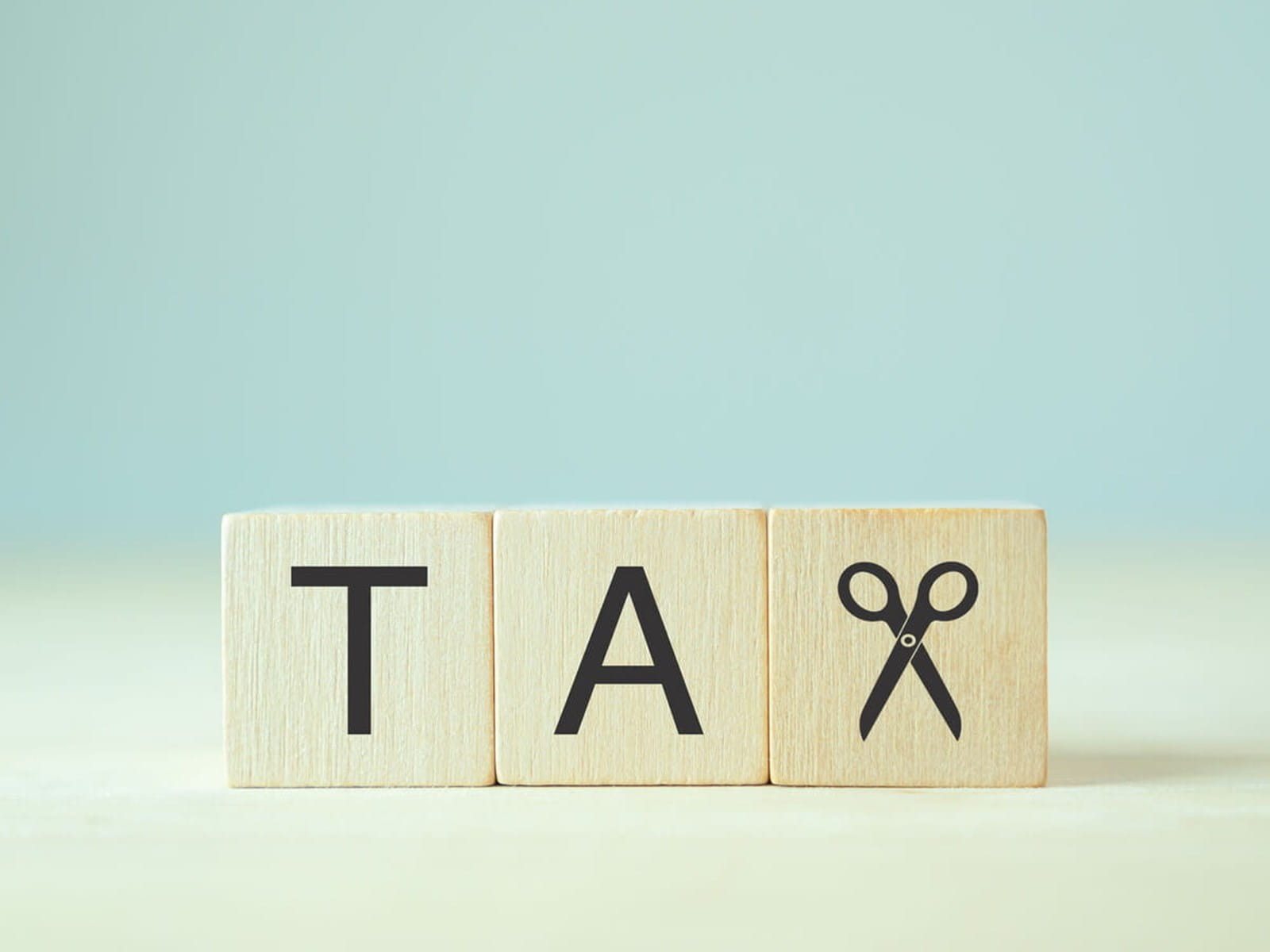 Wooden block spelling out the words Tax. The 'X' in the word is replaced with a pair of scissors representing tax cuts.